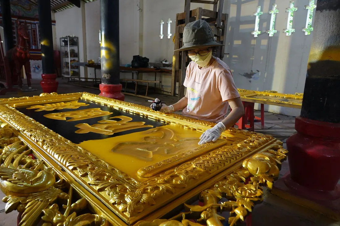 Ruce restaurátora pracující na zlacené ornamentální řezbě s bohatě členěným povrchem